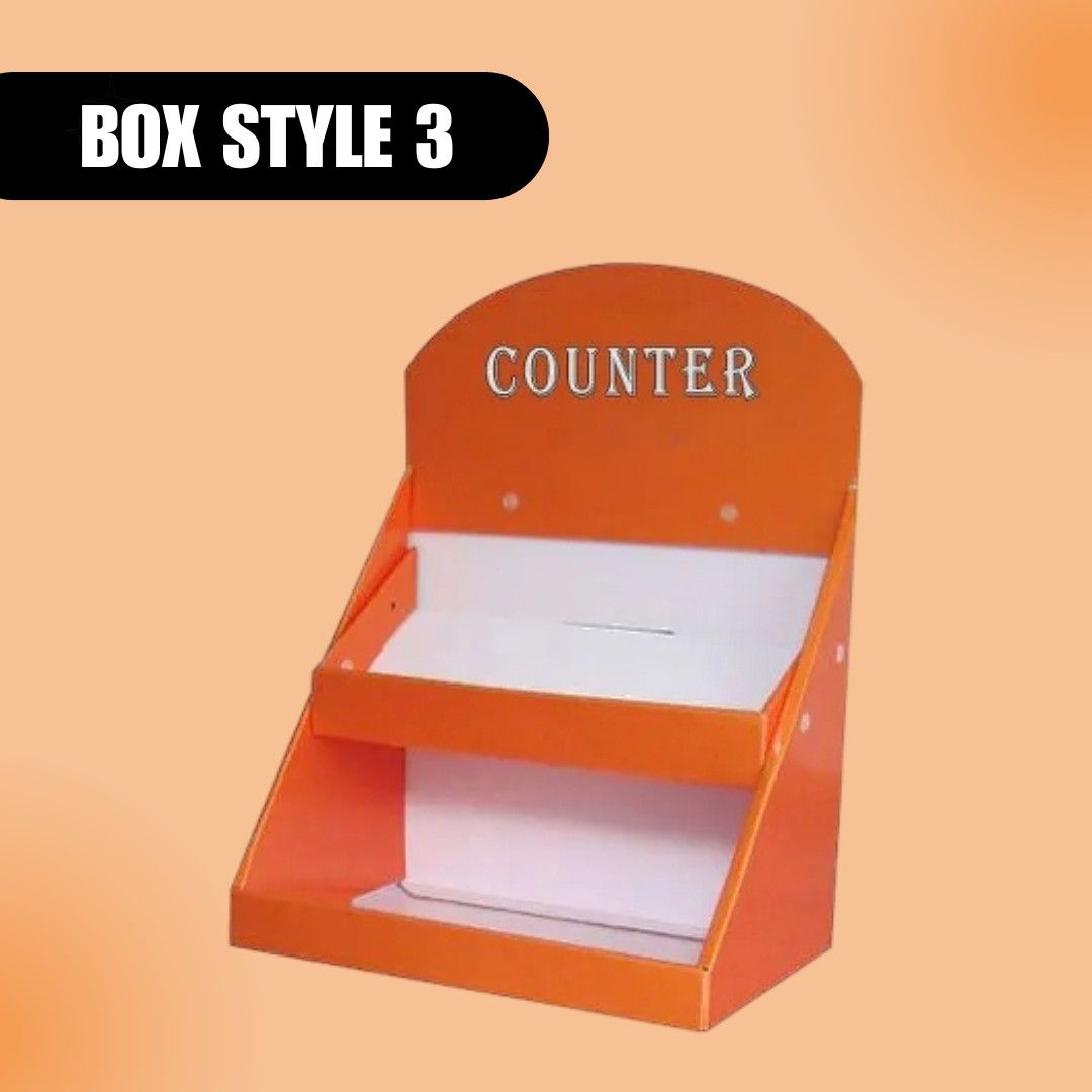 An orange countertop display box labeled "Counter" with two white shelves against a peach background. Bold text reads "Box Style 3." Modern and functional.