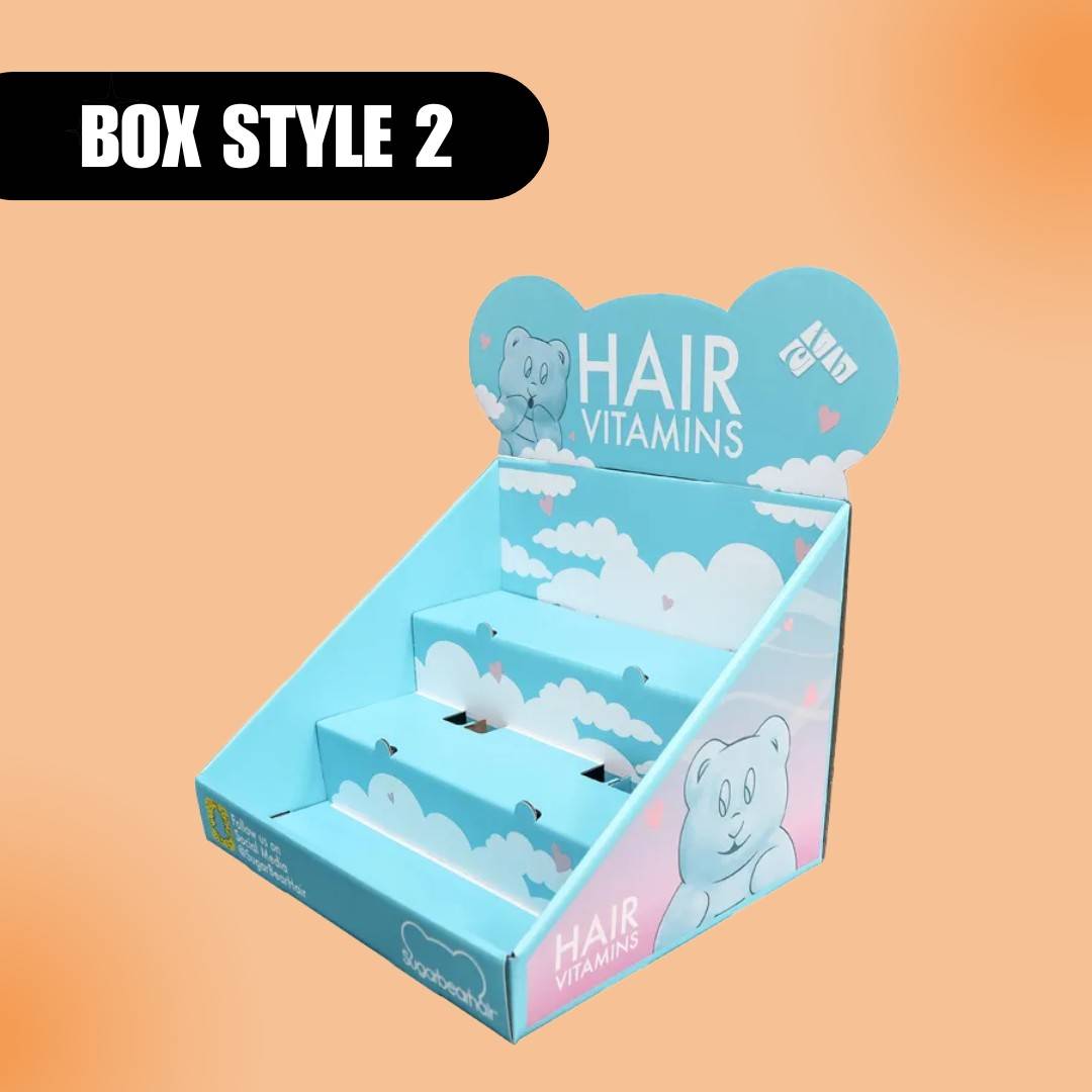 Display box for hair vitamins with a blue and white cloud design, featuring a teddy bear graphic. Labeled "Box Style 2" on a peach background.